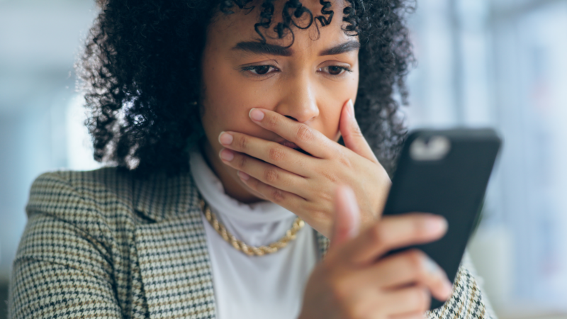 Person som reagerar chockat när hen läser ett misstänkt mejl på mobilen.
